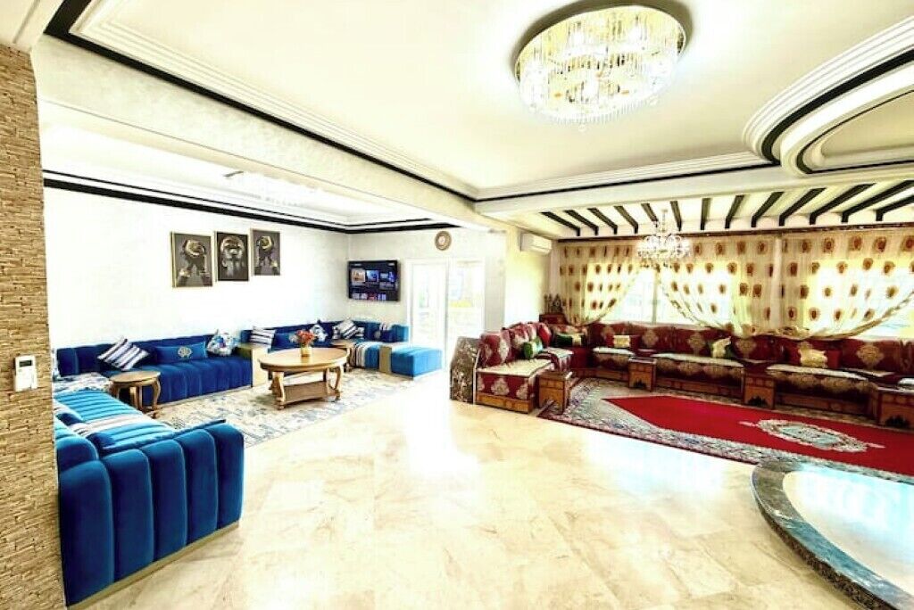 Un salon spacieux agrémenté d’un grand lustre, de canapés bleus et d’un tapis rouge.