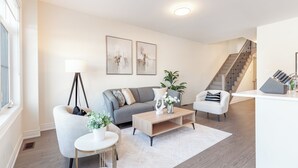 A modern living room with a grey sofa, a white armchair, a coffee table, and a floor lamp. There is a staircase leading to another level. - Modern Family Haven | 3BR Upstairs + Private Lower Suite (Richmond Hill)