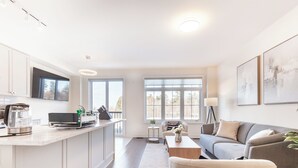 A modern kitchen with a built-in oven, a coffee machine, and a dining area with a sofa and a coffee table. - Modern Family Haven | 3BR Upstairs + Private Lower Suite (Richmond Hill)