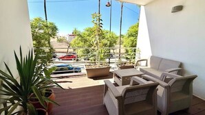 Un balcone con mobili in vimini, piante in vaso e vista su auto parcheggiate e alberi.