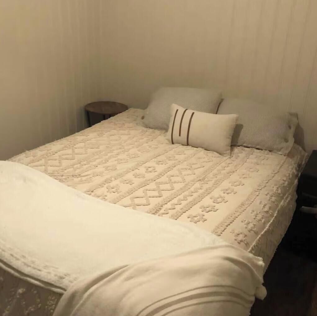 Un lit bien fait, avec une couvre-lit à motifs et des oreillers, une table de chevet et un mur orné de lignes verticales.