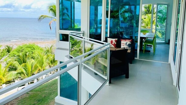 A modern balcony with a glass railing overlooking a beach and ocean.