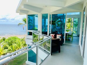 Un balcon moderne avec une balustrade en verre donnant sur une plage et l’océan.