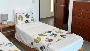 A bedroom with two single beds, a wooden dresser, a nightstand, and a wall-mounted lamp.