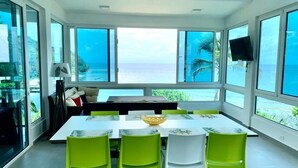A dining area with a large table and chairs, a television, and a view of the ocean.