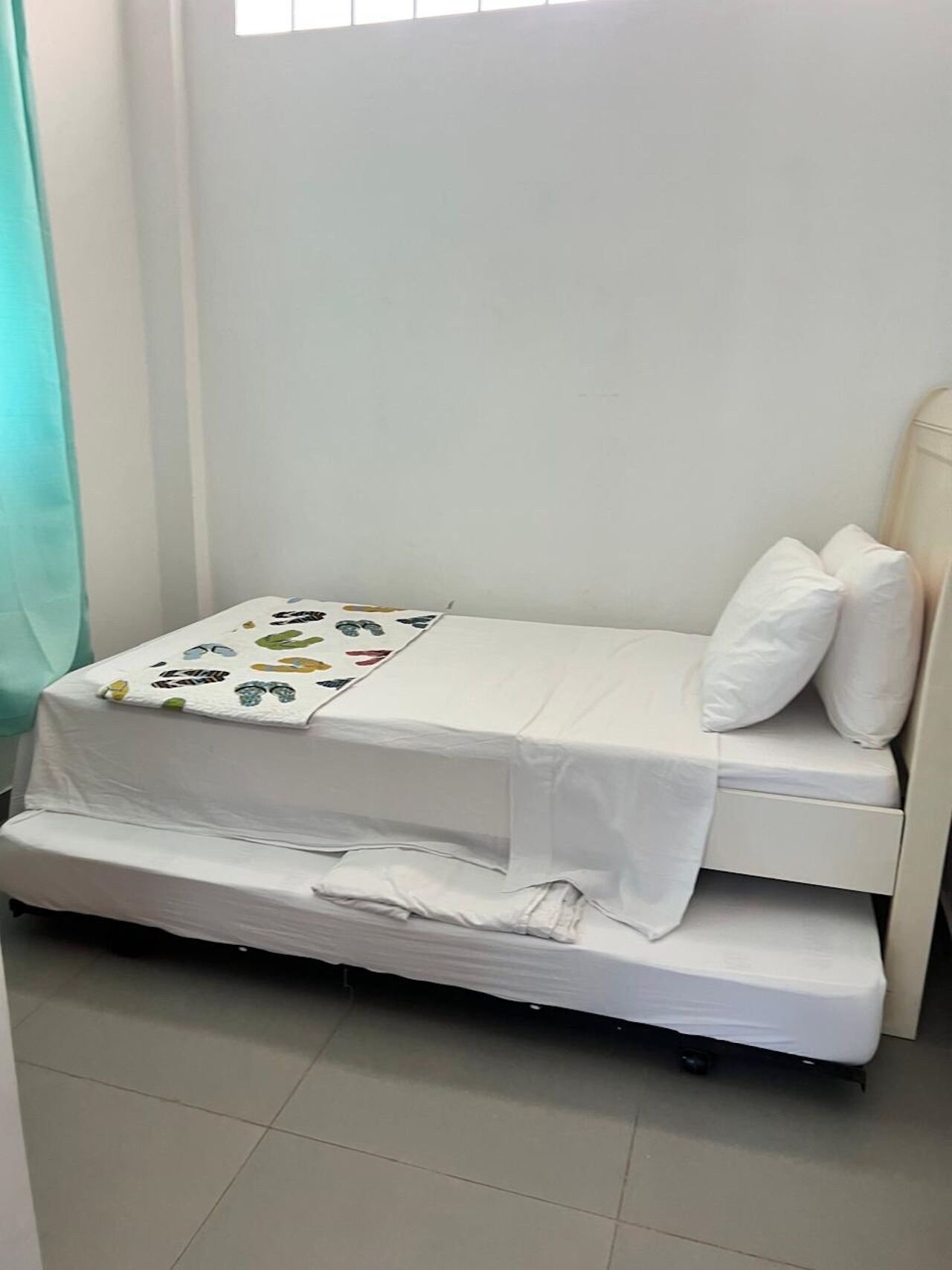 Une petite chambre avec un lit simple, une couette et des oreillers blancs, une fenêtre avec des stores et un rideau.