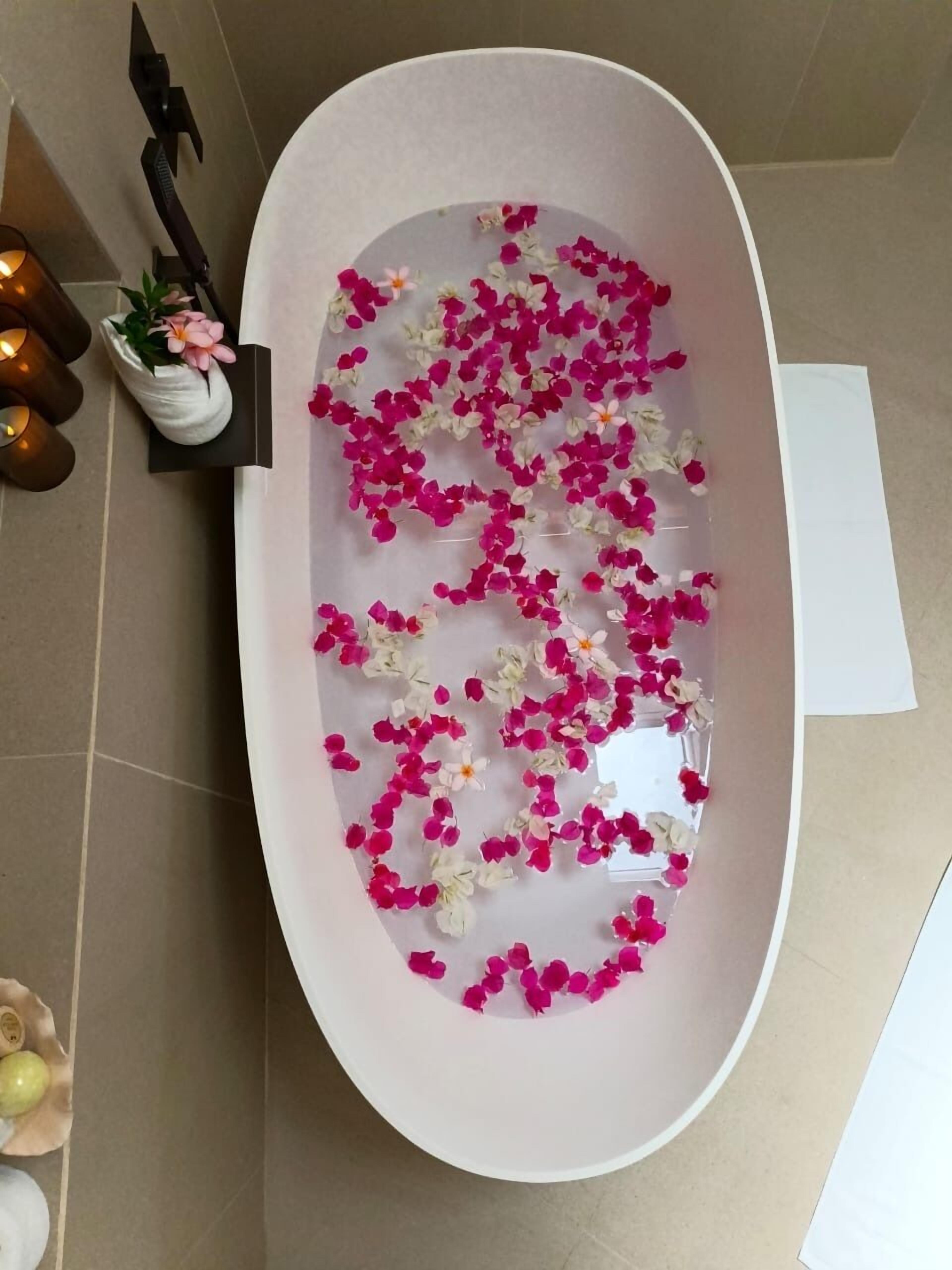 A bathtub filled with water and pink and white rose petals.