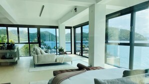 A modern bedroom with a large bed, a sofa, and a dining area with a view of the water. - The Waterfront Studio (Busuanga)