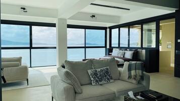 A modern living room with a large window, a sofa, a coffee table, and a bed with a view of the sea.