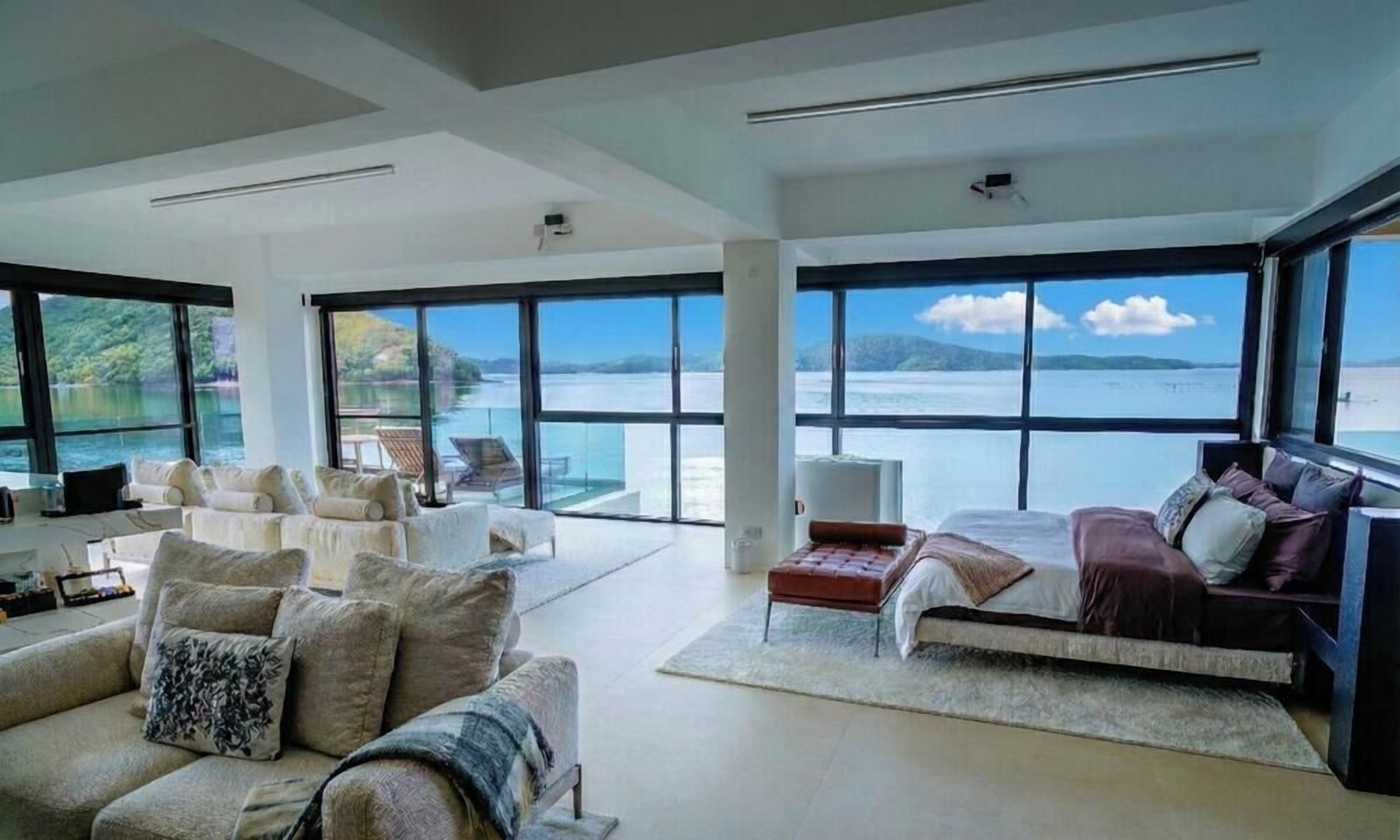 A spacious living area with large windows, a sofa, a bed, and a view of a body of water.