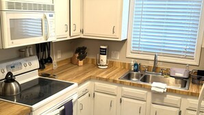 A kitchen with white cabinets, a microwave, stove, sink, and a window with blinds. - The Blue Turtle: 3-bedroom, 2-bath MB townhouse w/ 5 min walk to the beach (Myrtle Beach)
