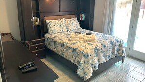 Een slaapkamer met een bed, een nachtkastje, een bureau en een stoel. Er liggen twee afstandsbedieningen op het bureau.