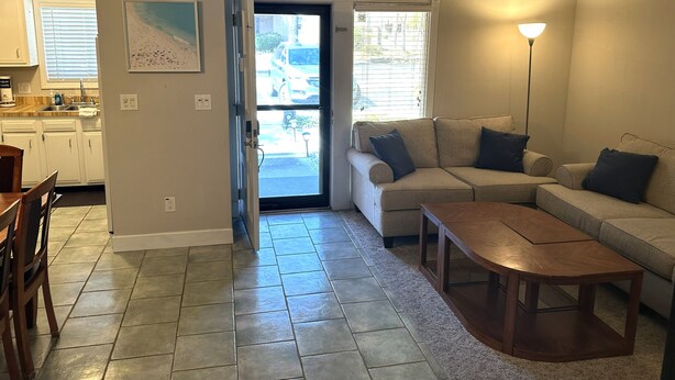 A living room with a sofa, a coffee table, and a dining area with chairs. There is a kitchen visible through an open door. - The Blue Turtle: 3-bedroom, 2-bath MB townhouse w/ 5 min walk to the beach (Myrtle Beach)