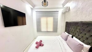 A neatly made bed with white and pink linens, a flat-screen TV mounted on the wall, and a window with blinds. - Charming furnished apartment (Wifi Fiber 100 Mb) (Fès)
