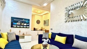 A modern living room with a blue sofa set, a glass coffee table, and a decorative wall piece. - Charming furnished apartment (Wifi Fiber 100 Mb) (Fès)