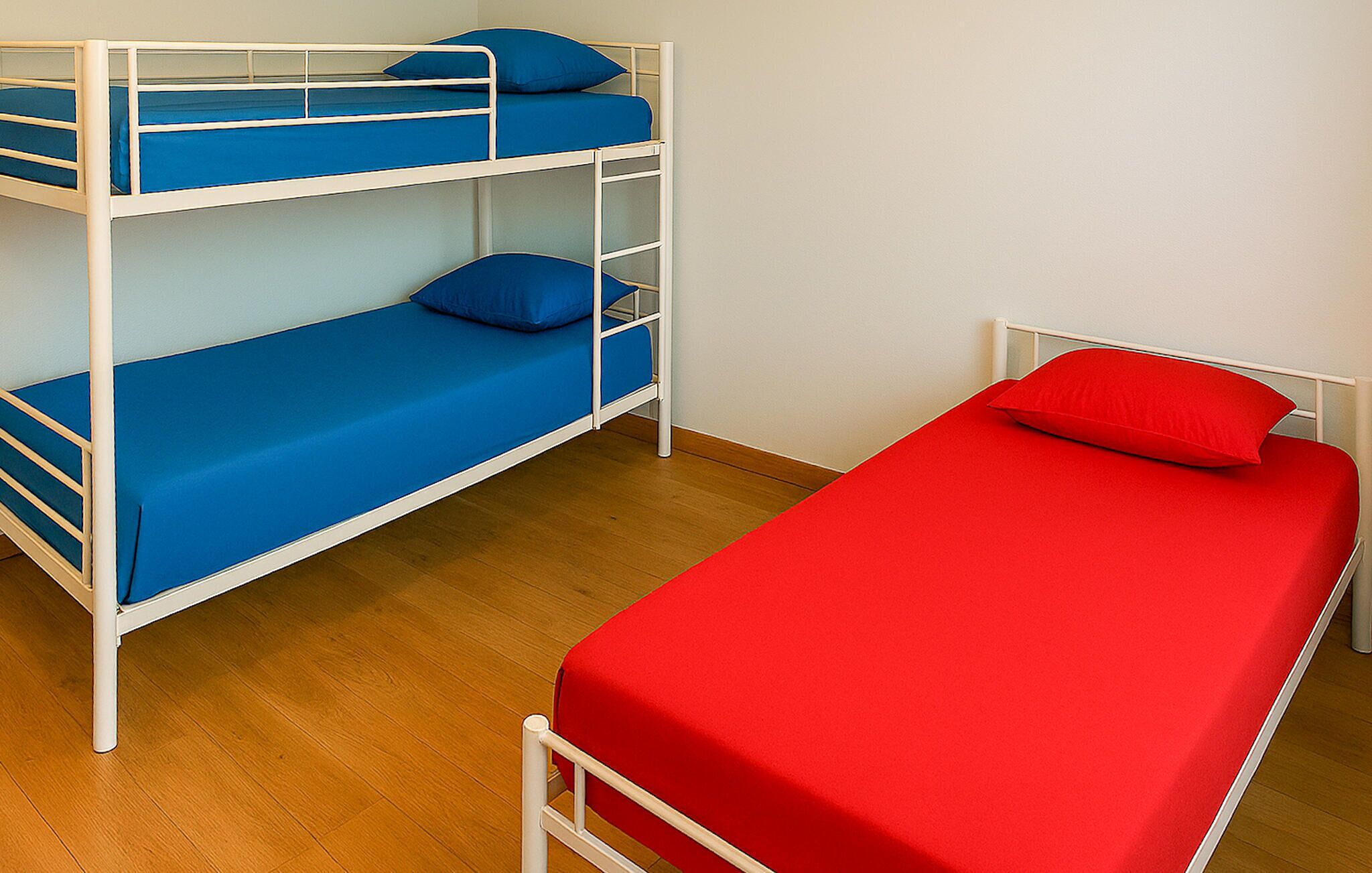 A bunk bed with blue bedding and a single bed with red bedding.