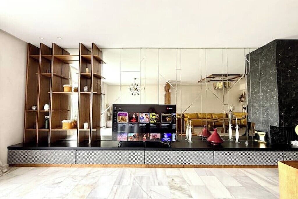 A modern living room with a large flat-screen TV, wooden shelving, and a marble floor.