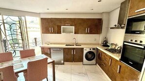 A modern kitchen with a built-in washer and dryer, a dining area with wicker chairs, and a large oven. - AR Apartments (Park view-Wifi 200Mb) (Fès)