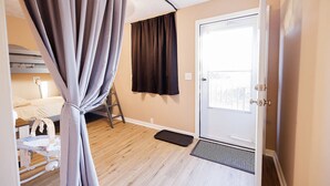 Ein Schlafzimmer mit einem Bett, einer Leiter, einem Fenster mit Vorhängen, einer Tür und einer kleinen Matte.