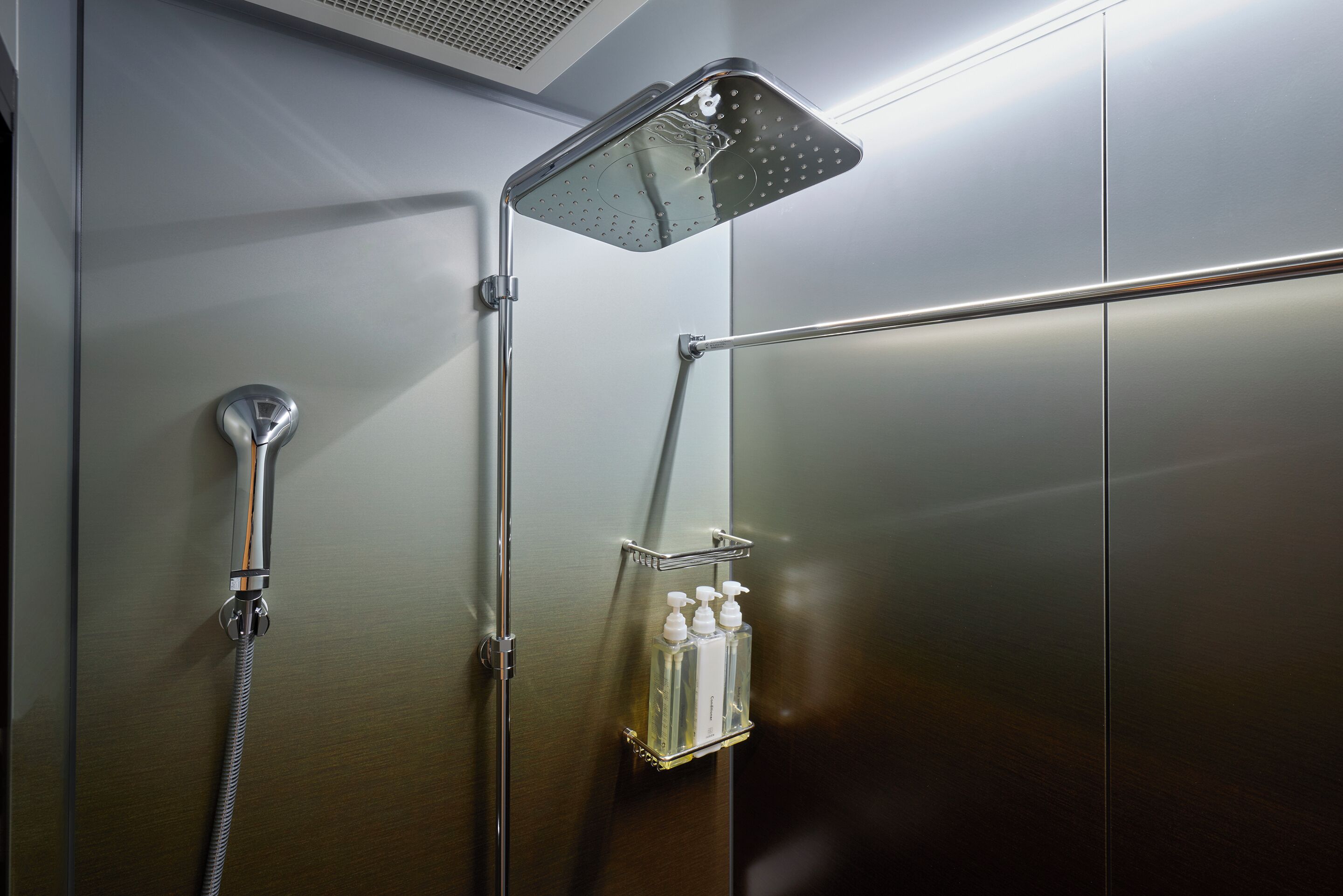 A shower with a handheld showerhead, a wall-mounted faucet, and a soap dispenser.