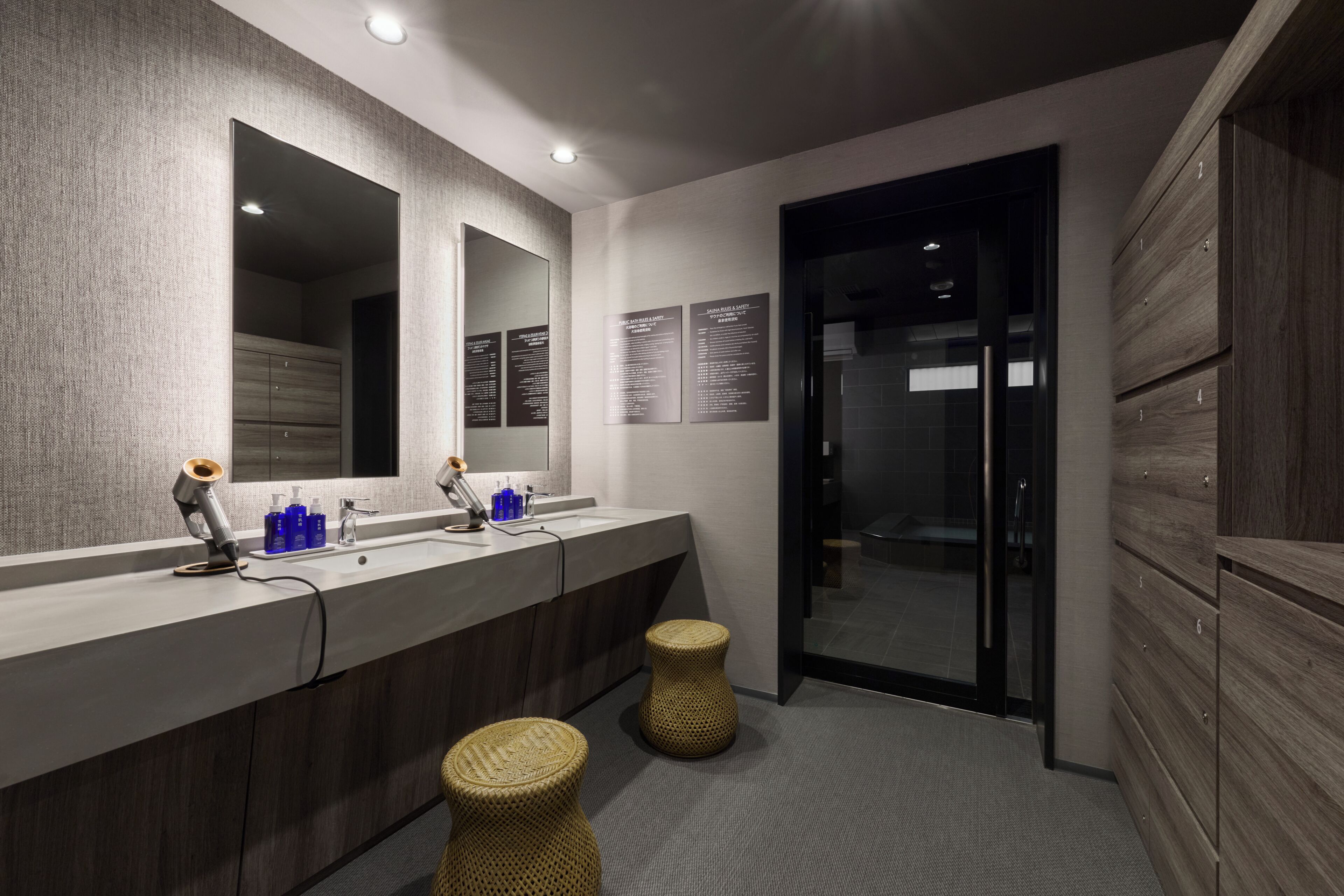 A modern bathroom with a large mirror, wooden cabinets, a sink, and two woven stools.