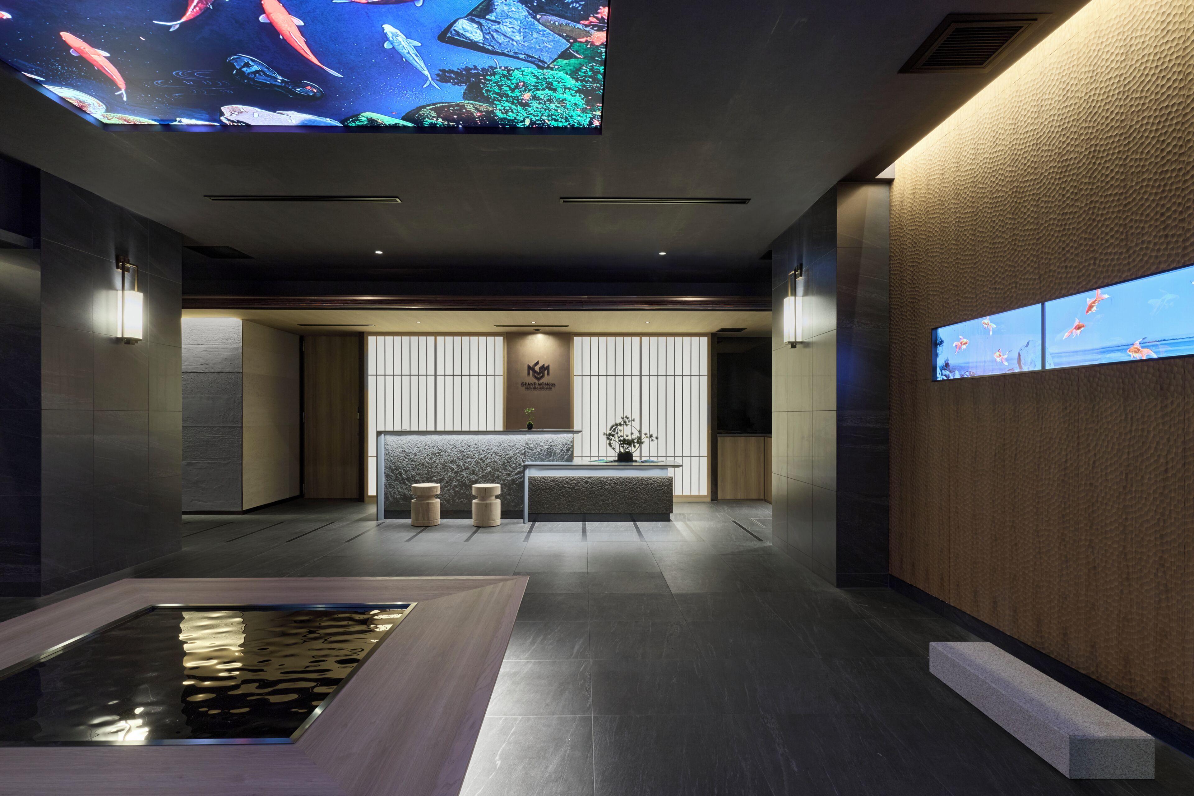 A modern lobby with a reception desk, a koi pond, and a large digital screen displaying fish.