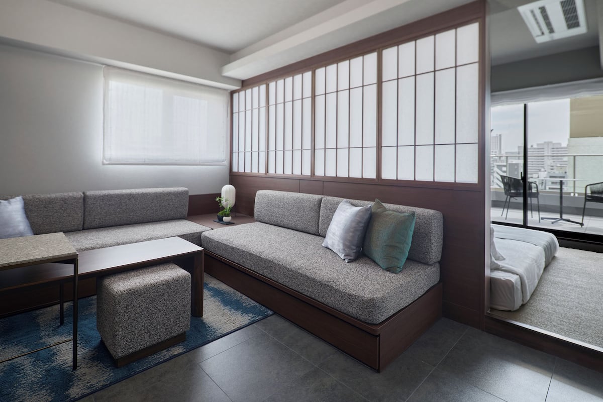 A modern living room with a sofa, a coffee table, and a view of the city through large windows.