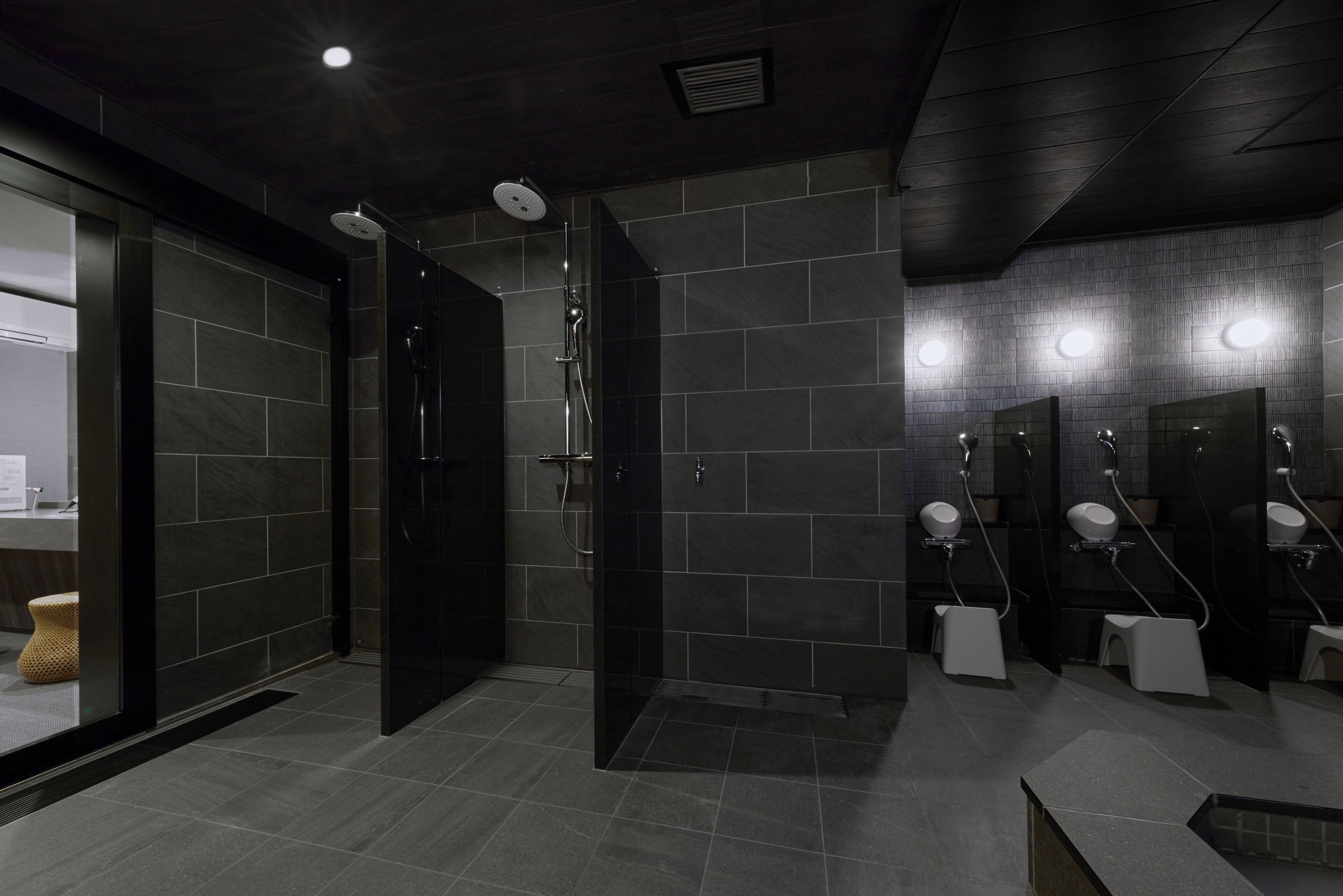 A modern bathroom with dark tiles, a glass shower enclosure, and multiple sinks.