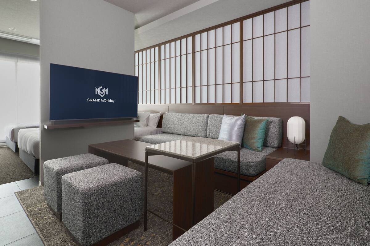 A modern hotel room with a sofa, ottomans, a TV, and a large window with a view.