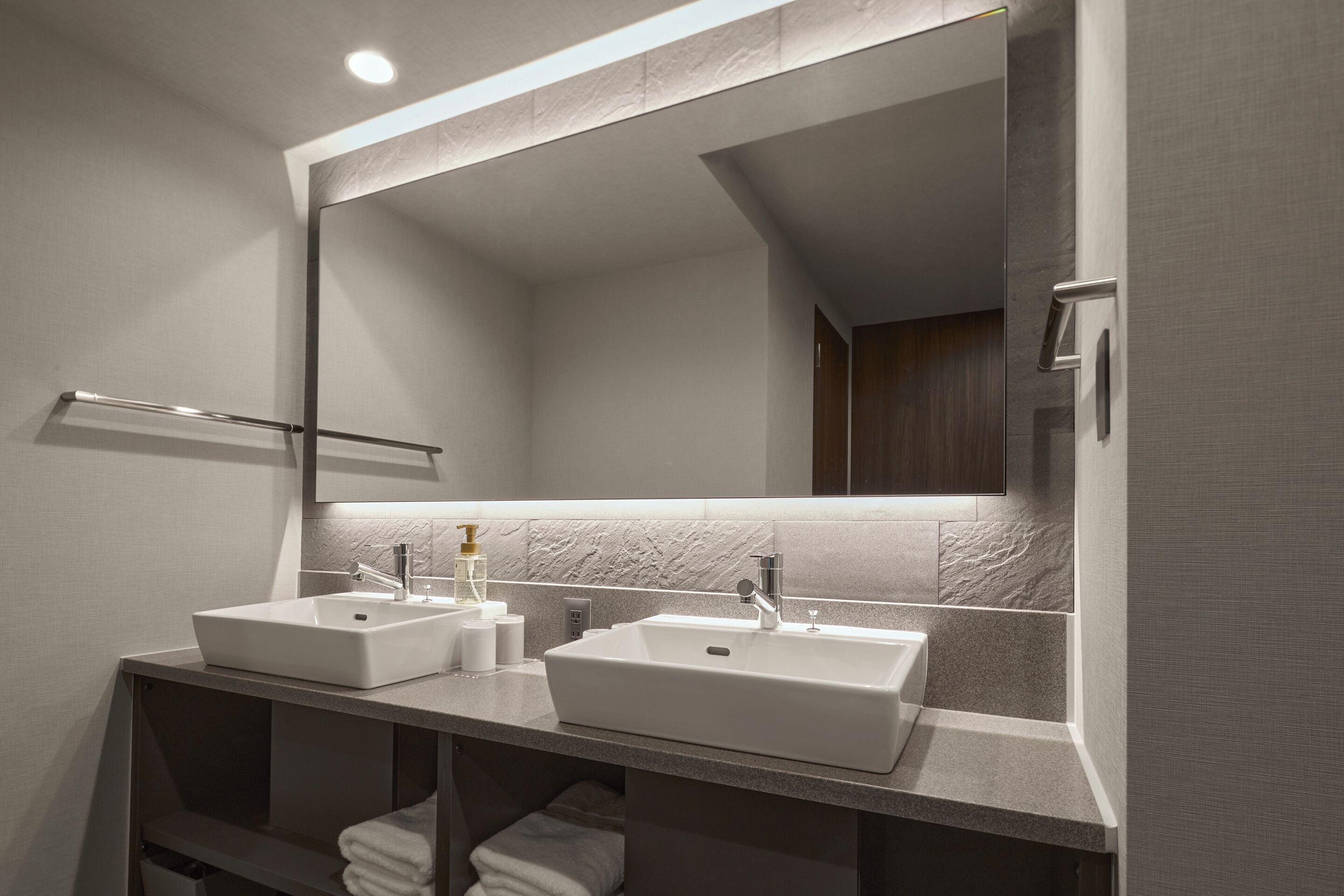 A modern bathroom with two sinks, a large mirror, and a towel rack.