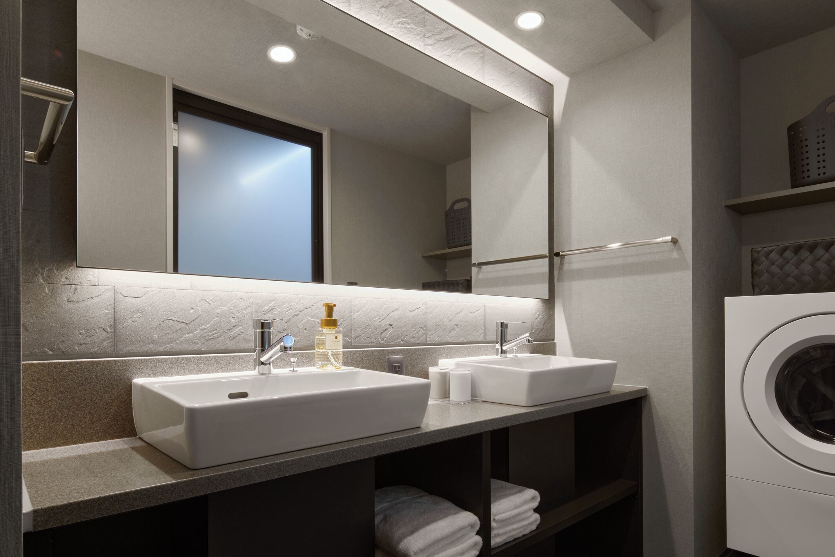 A modern bathroom with two sinks, a mirror, a towel rack, and a washing machine.