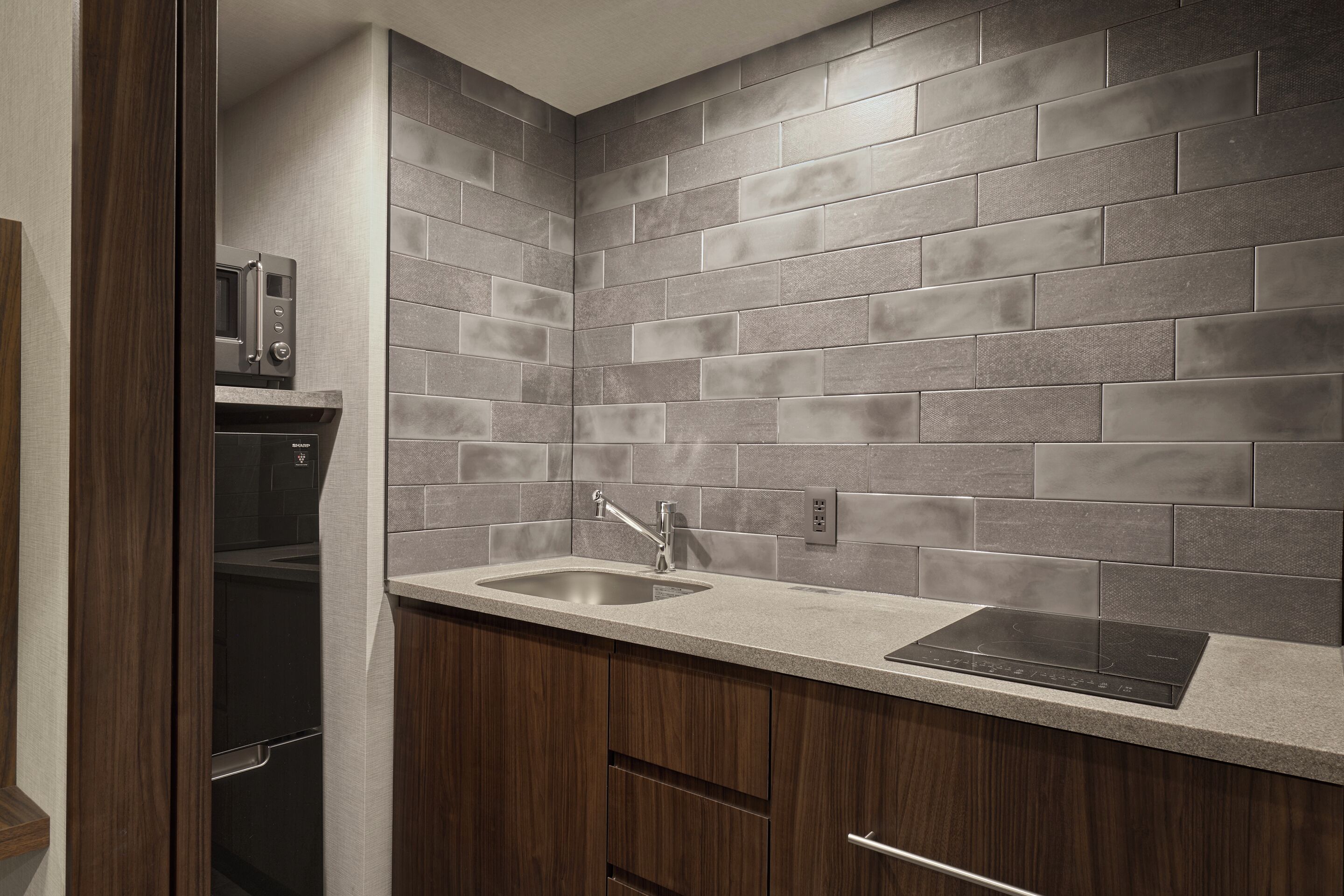 A kitchen with grey tiled backsplash, a stainless steel sink, and a built-in microwave.