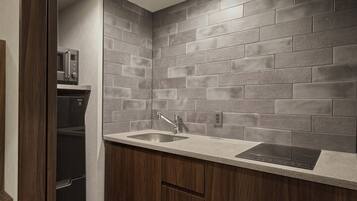 A kitchen with grey tiled backsplash, a stainless steel sink, and a built-in microwave.