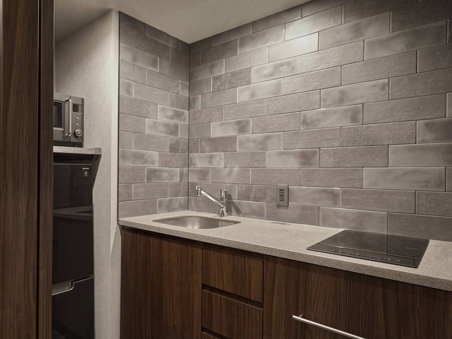 A kitchen with grey tiled backsplash, a stainless steel sink, and a built-in microwave.