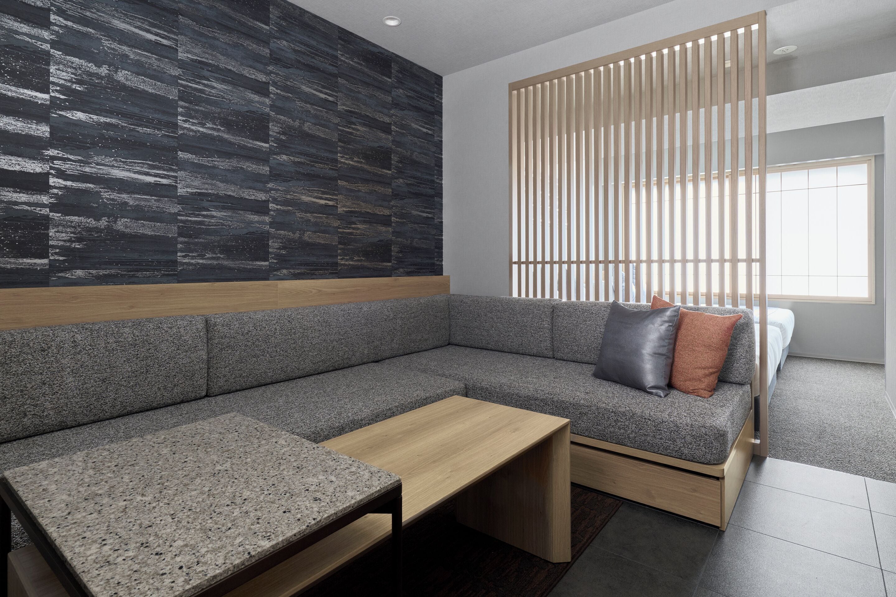 A modern living room with a grey sectional sofa, a wooden coffee table, and a black textured wall.