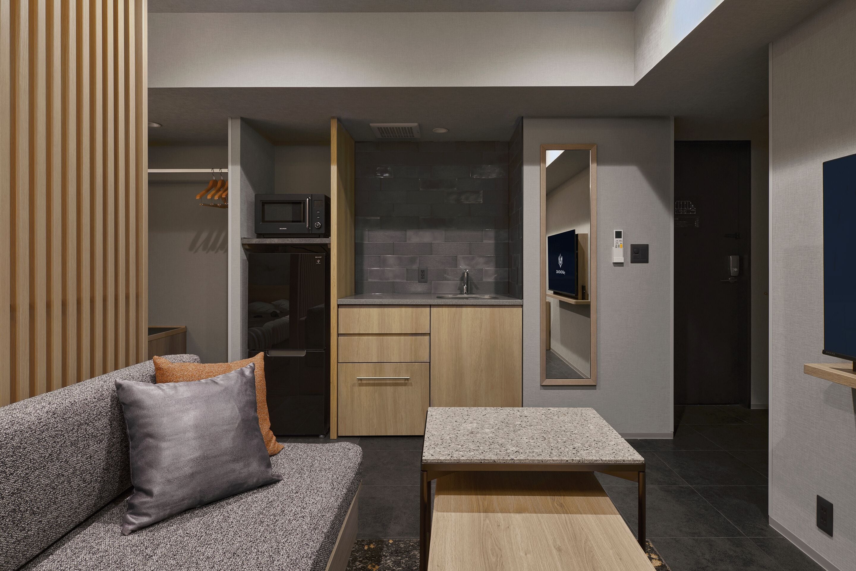 A compact living space with a sofa, a small table, a kitchenette, and a mirror.