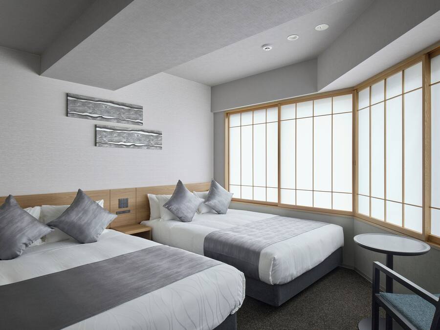 A hotel room with two beds, a small round table, and a large window with wooden frames.