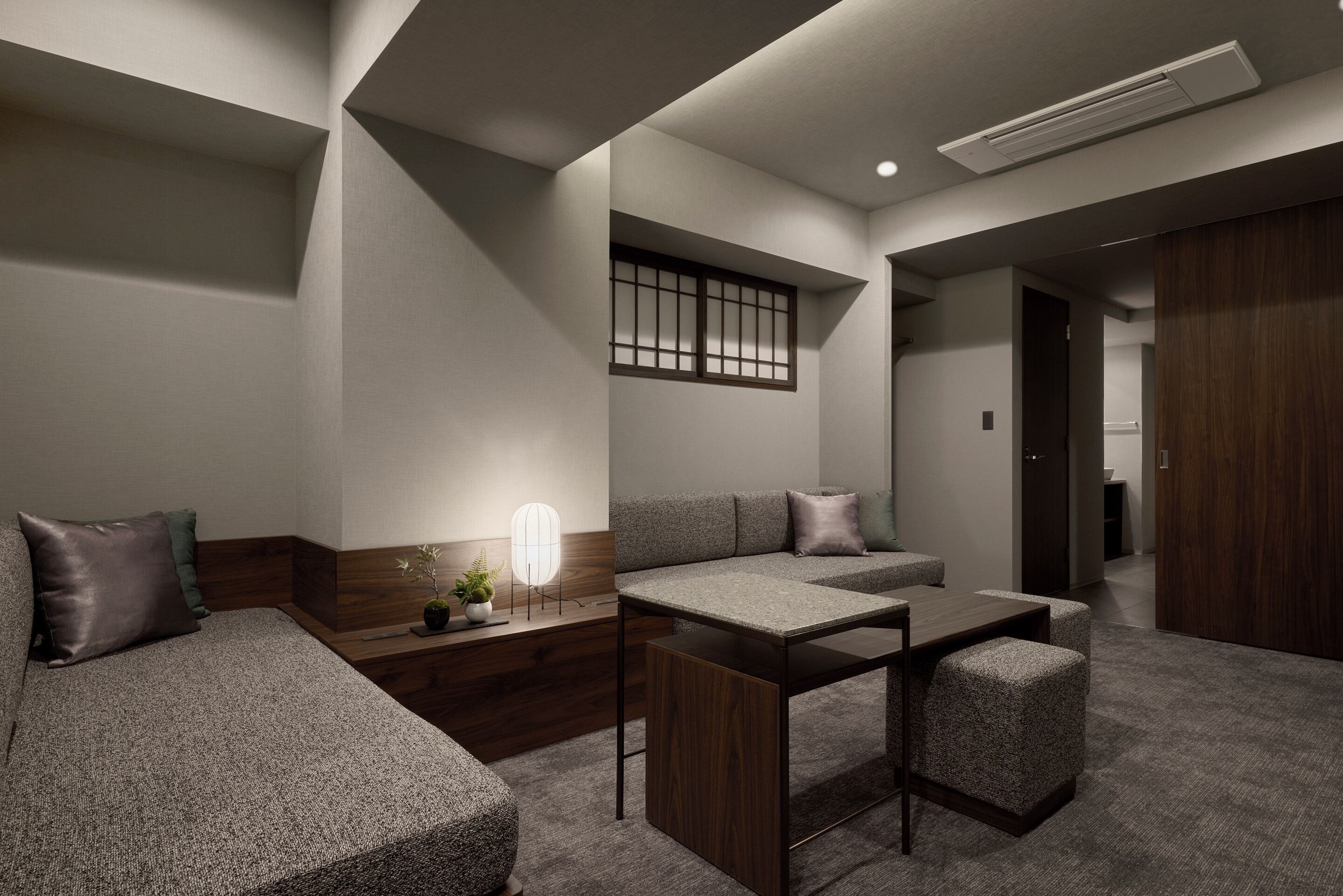 A modern hotel room with a sofa, a small table, a decorative light, and a window with a view.