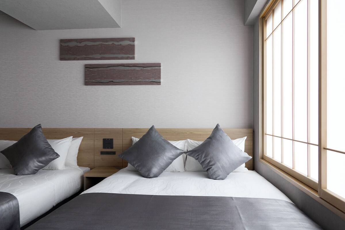 A hotel room with two beds, a wooden headboard, a large window, and two wall-mounted artworks.
