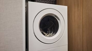 A front view of a modern, white washing machine in a room with a wooden panel and a textured wall.