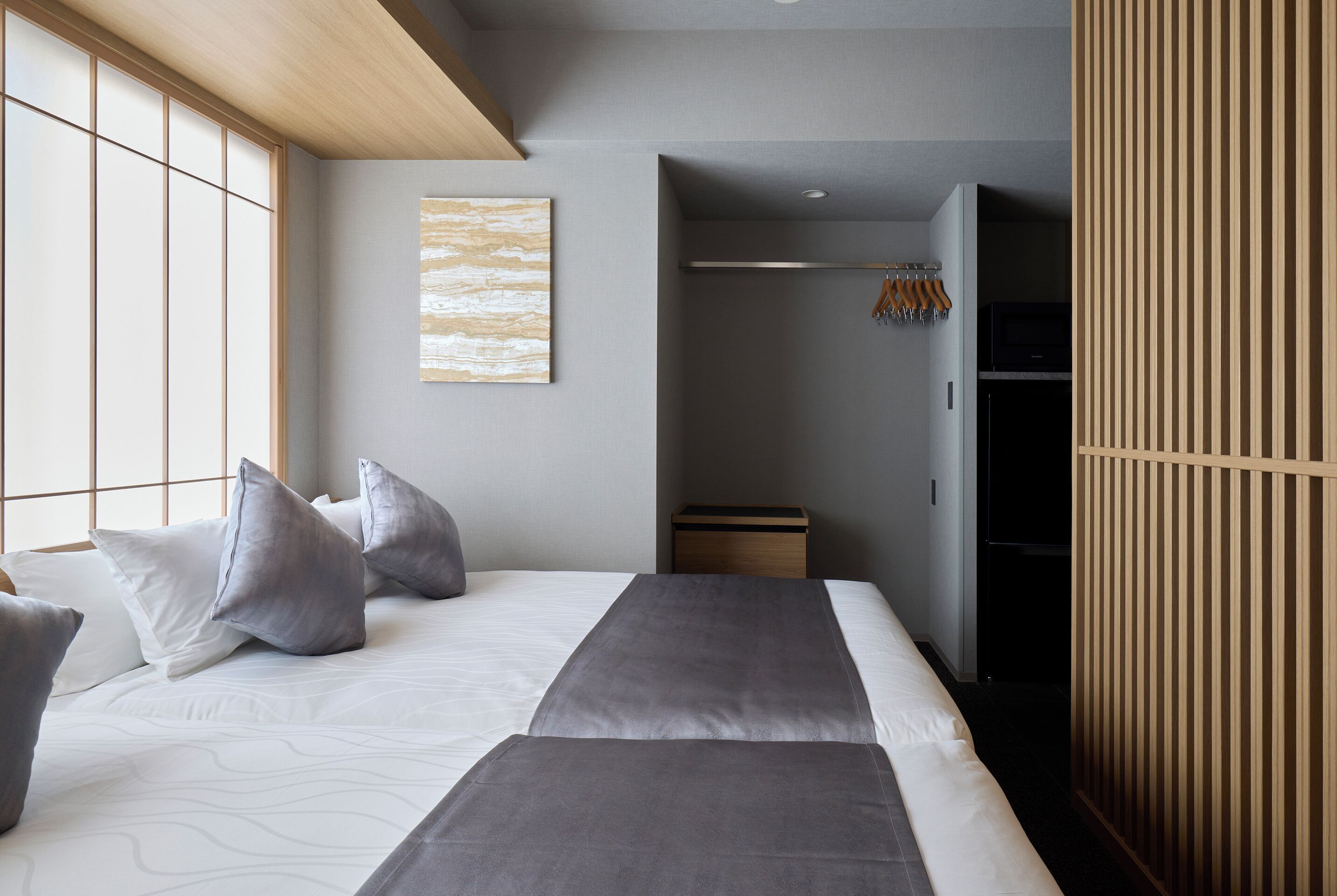 A modern hotel room with a large bed, a wardrobe, and a small walk-in closet.