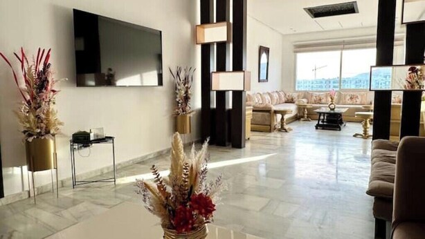 A spacious living area with a flat-screen TV mounted on the wall, a sofa set, and a coffee table with decorative plants. - AR Apartments downtown (Wifi 200 Mb) (Fès)