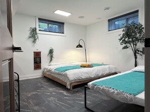 Et moderne værelse med to senge, en loftlampe, en plante på væggen og et vindue med persienner.