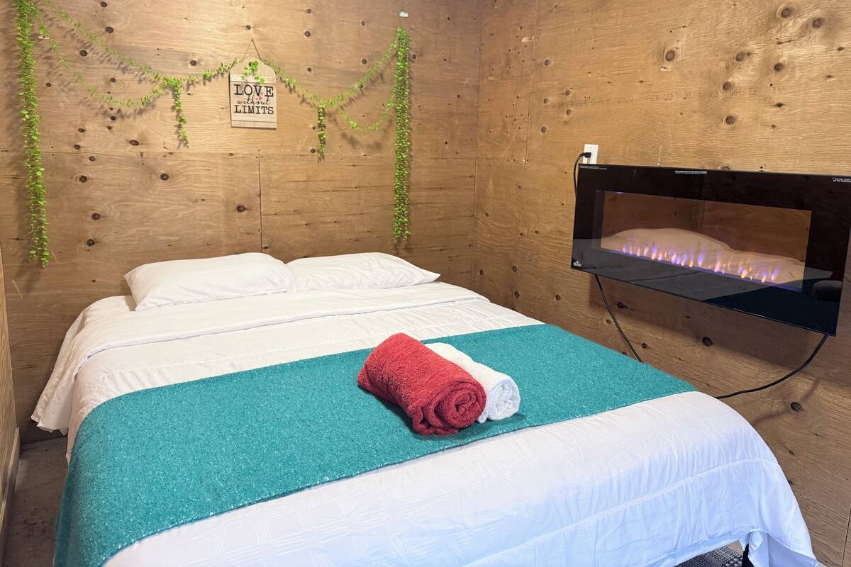 A wooden room with a bed, a wall-mounted TV, and a sign with a motivational quote.
