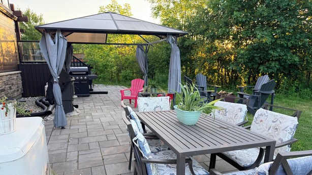 An outdoor patio with a table and chairs, a grill, and a covered seating area.