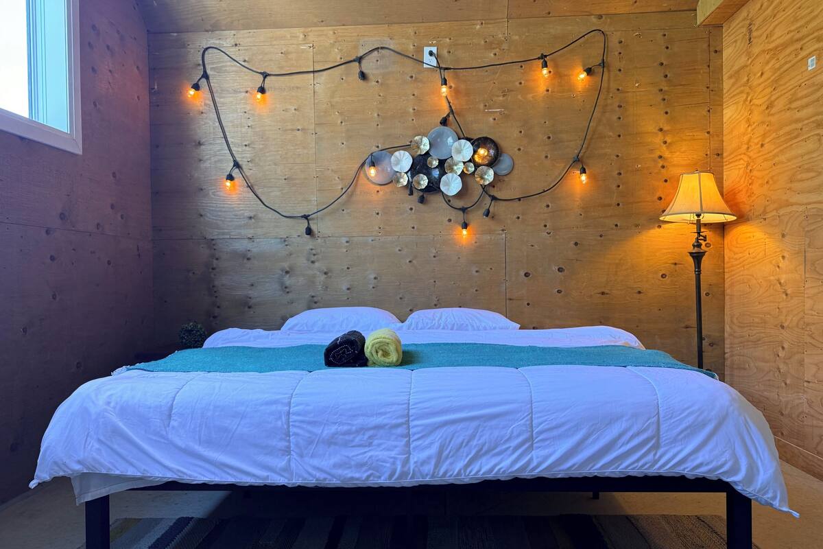A wooden-paneled room with a bed, string lights, and a lamp.