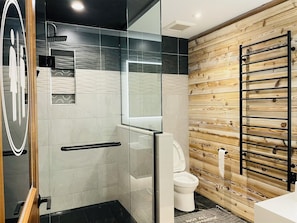 Ein modernes Badezimmer mit Duschkabine aus Glas, einer weißen Toilette und einer Holzvertäfelung.