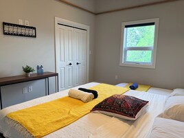 Quarto com cama, janela, porta, cabideiro e uma pequena mesa com uma planta.