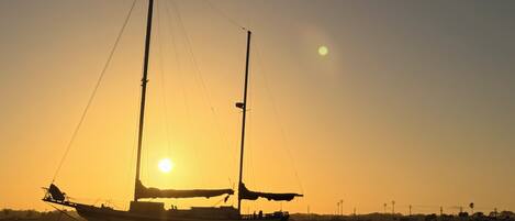 A boat with two masts sailing on calm waters during sunset.
