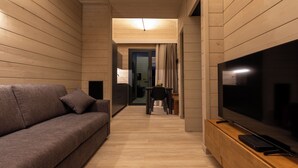 A modern living room with a sofa, a TV on a wooden stand, and a hallway leading to a kitchen area. - The Village Chalet (Castel di Sangro)